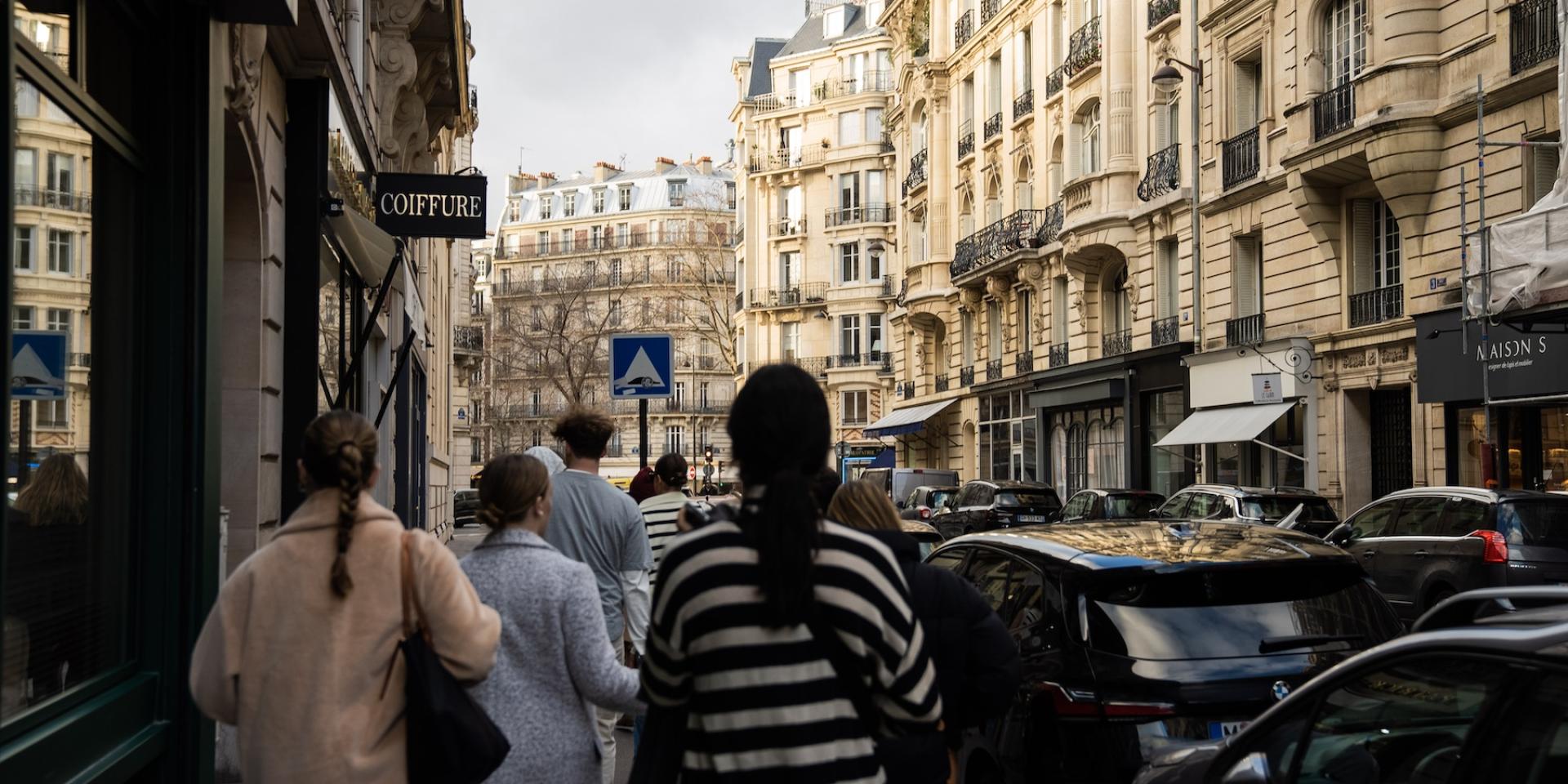 Students walk down a Paris street past a hairdressers